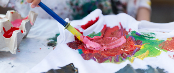 Bild på någon som målar med en pensel och använder färgerna rosa, gul, grön med flera.