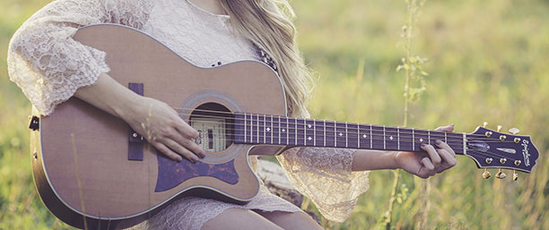Tjej som sitter ute i gräset och spelar guitarr.