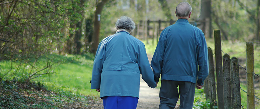 Äldre par på promenad på en stig i en grön skog