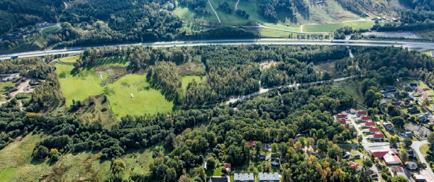 Flygfoto över Rinnaområdet med skog, bebyggelse och motorväg.