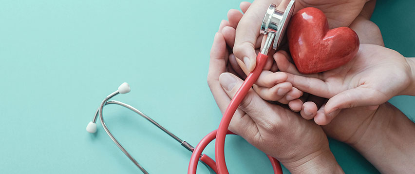 Händer som håller ett stetoskop som lyssnar på ett rött keramikhjärta.