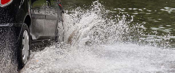Bil som kör igenom högt vatten efter översvämning.