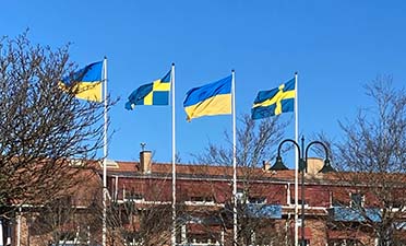 Svenska och ukrainska flaggor vid kommunhuset vajar mot en blå himmel.