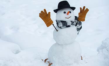 En snögubbe med morot till näsa, svart hatt och bruna handskar på pinnar till armar.